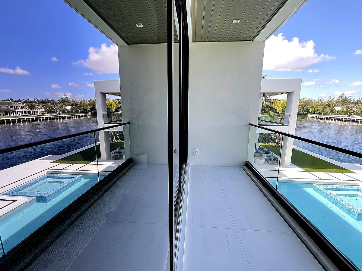 Impact glass corner reflecting pool and blue sky at South Florida waterfront home