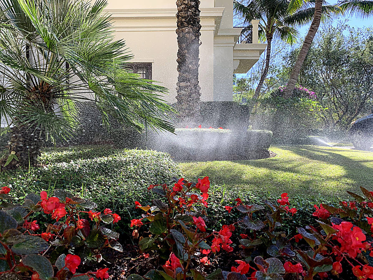 Irrigation system seasonal adjustment sprinkler mist over manicured lawn and flower beds South Florida