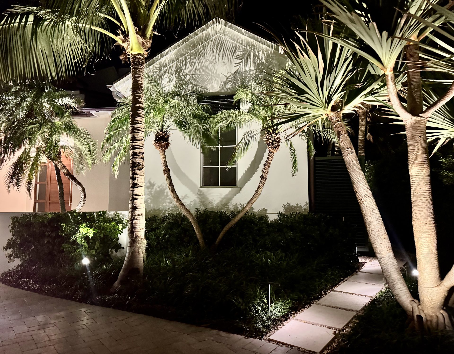 South Florida home facade with landscape lighting on palm trees and stepping stones
