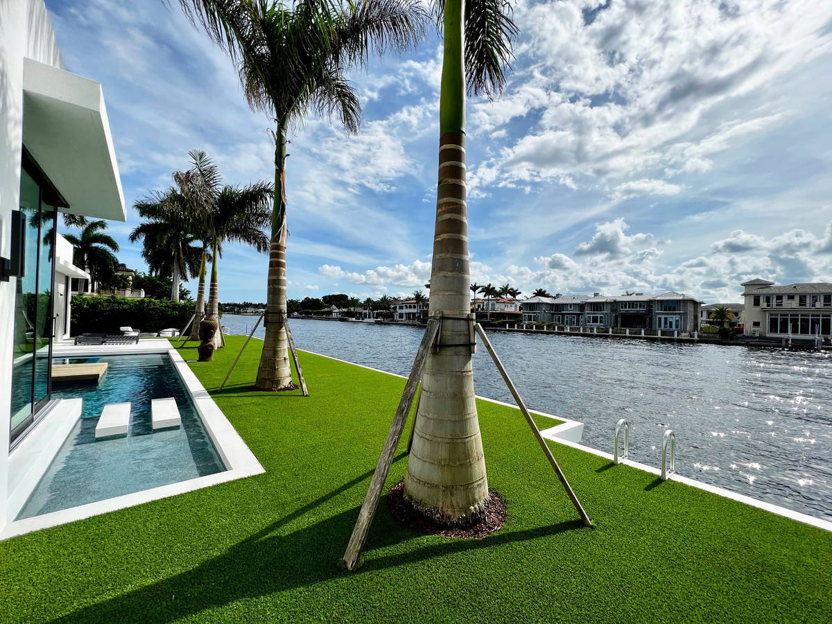 Florida Boys crew mowing a Lighthouse Point canal-front lawn with a boat on the lift